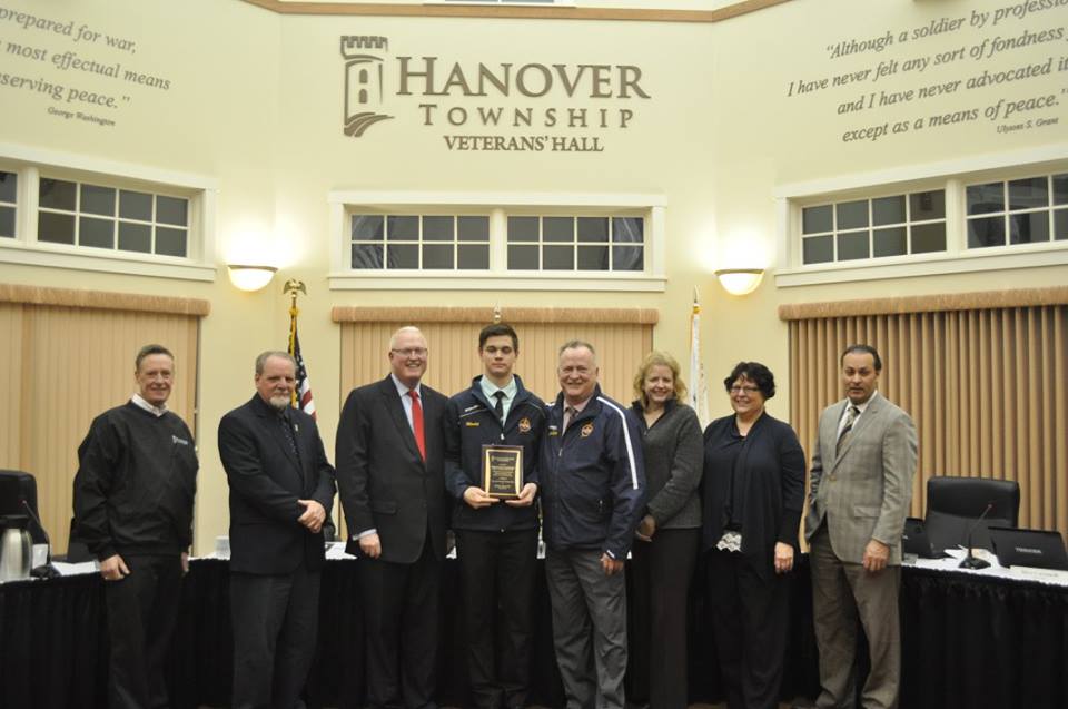 Six men and two women stand and smile while the man in the middle holds a plaque.