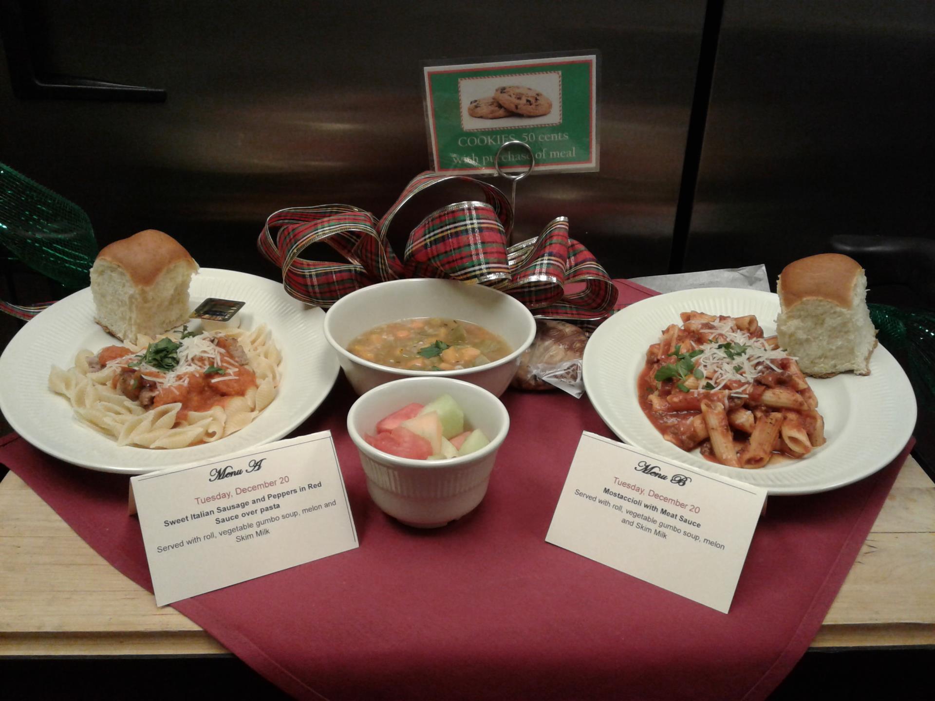 Two plates of pasta displayed on a red table with a bowl of soup and cup on fruit.