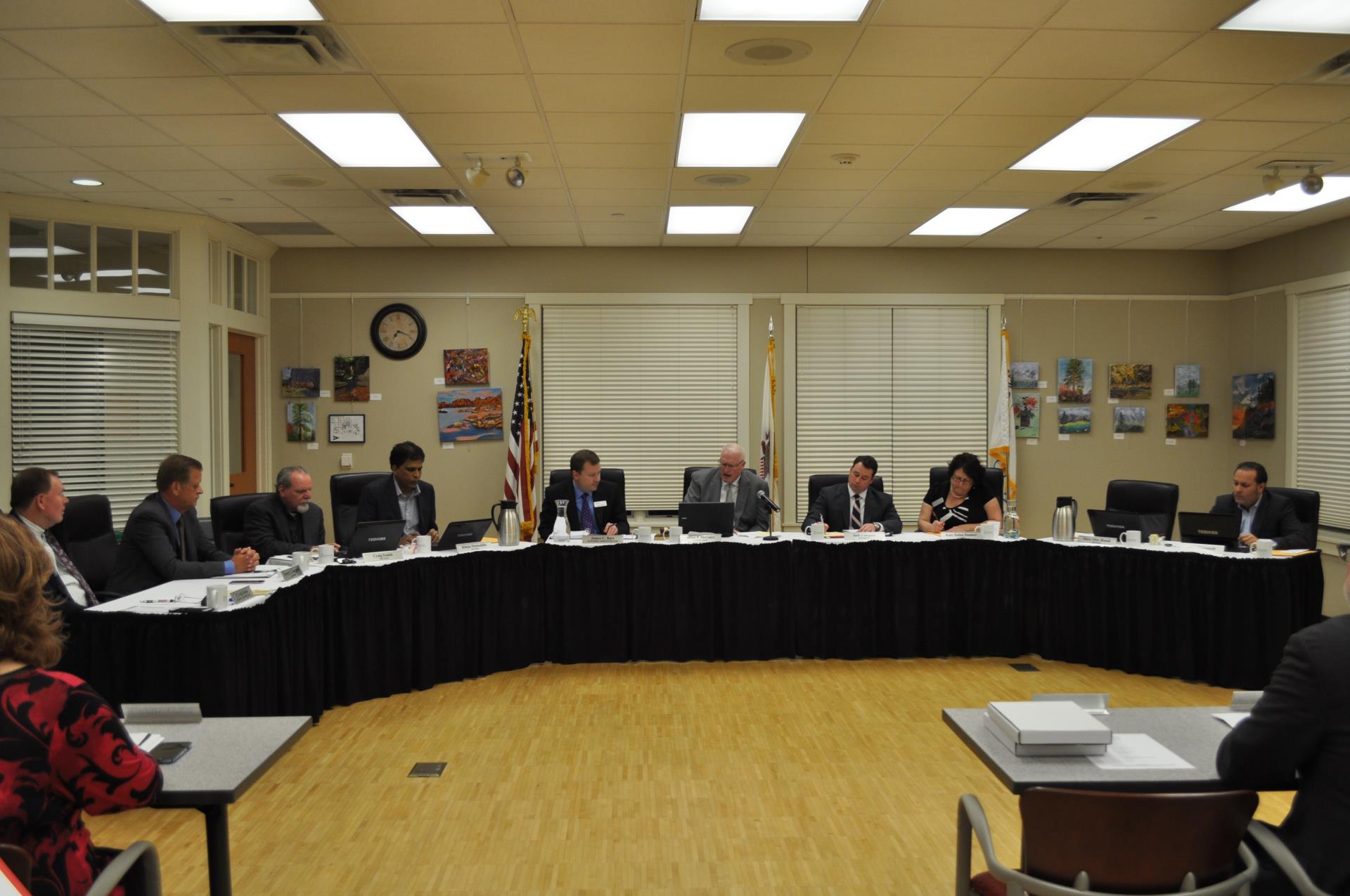 Seven men and one woman sit around table at board meeting.