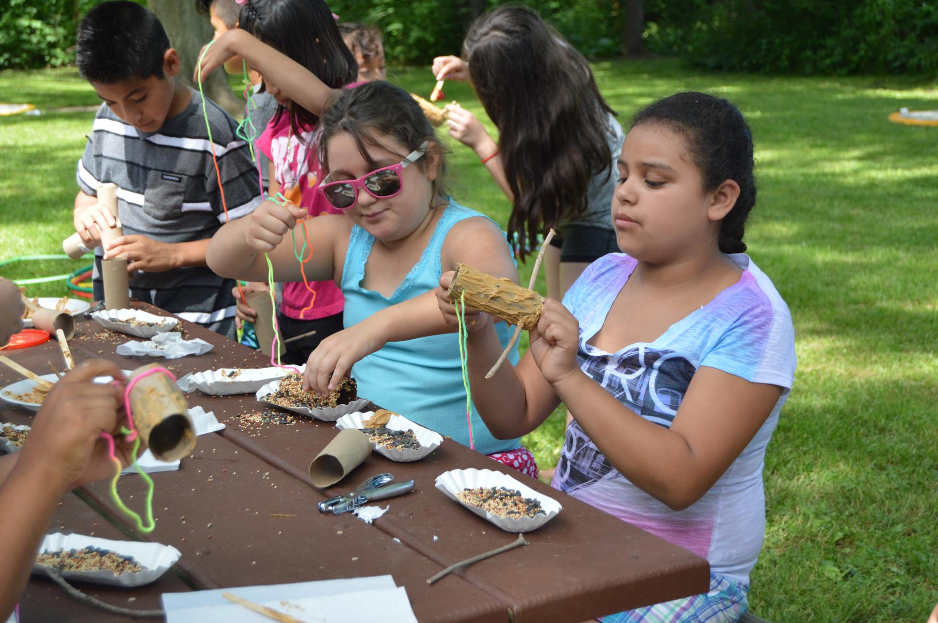 Kids making a messy craft on a picnic table at a park on a nice day.