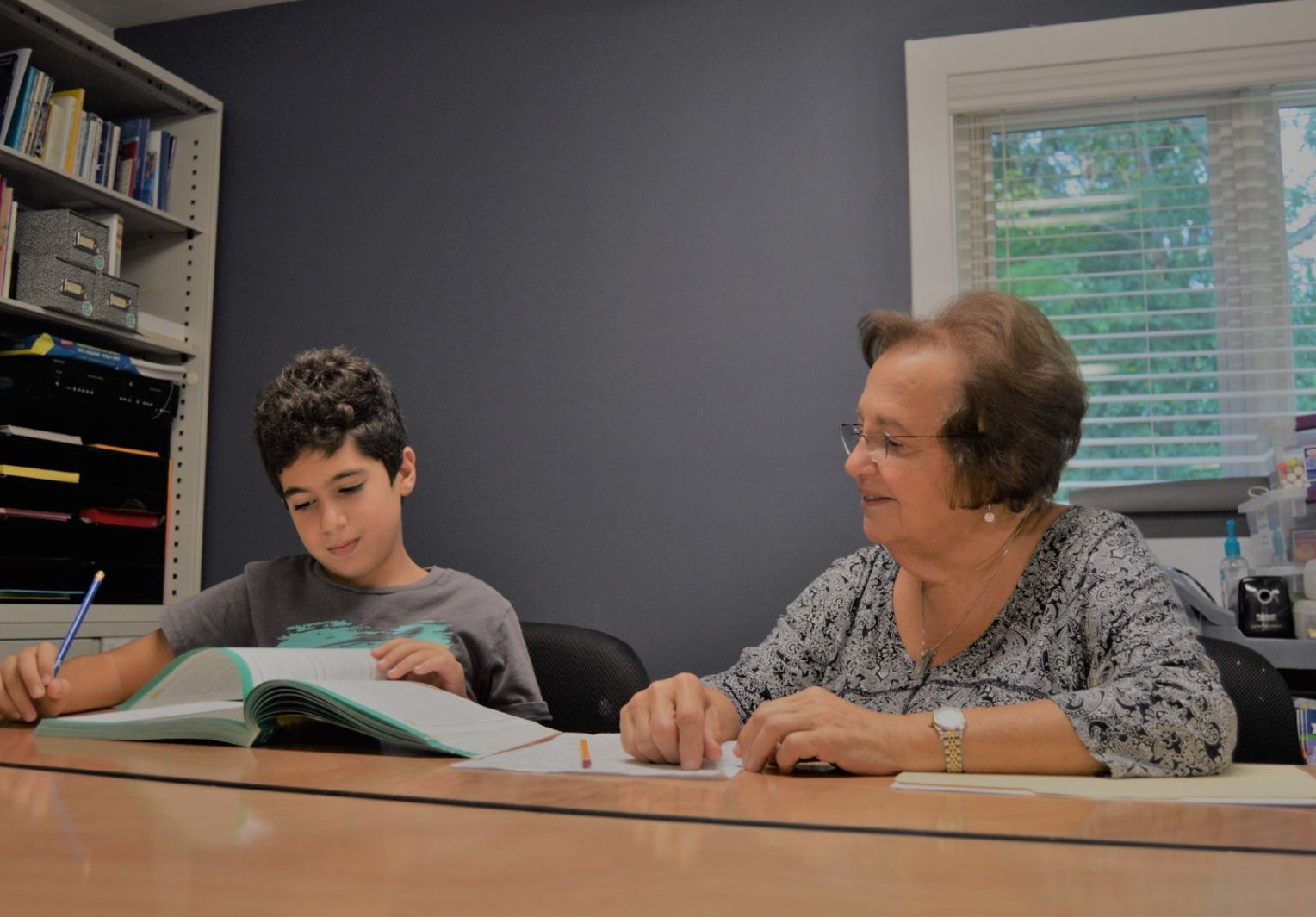 A Township tutor sitting at a table with a student providing assistance with math work.