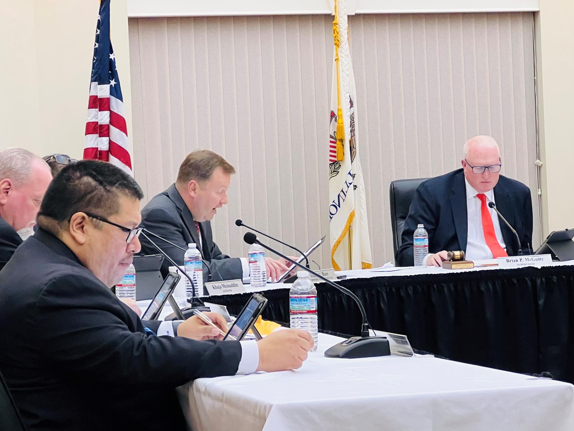 Officials and staff sitting at tables presenting a report during the meeting.