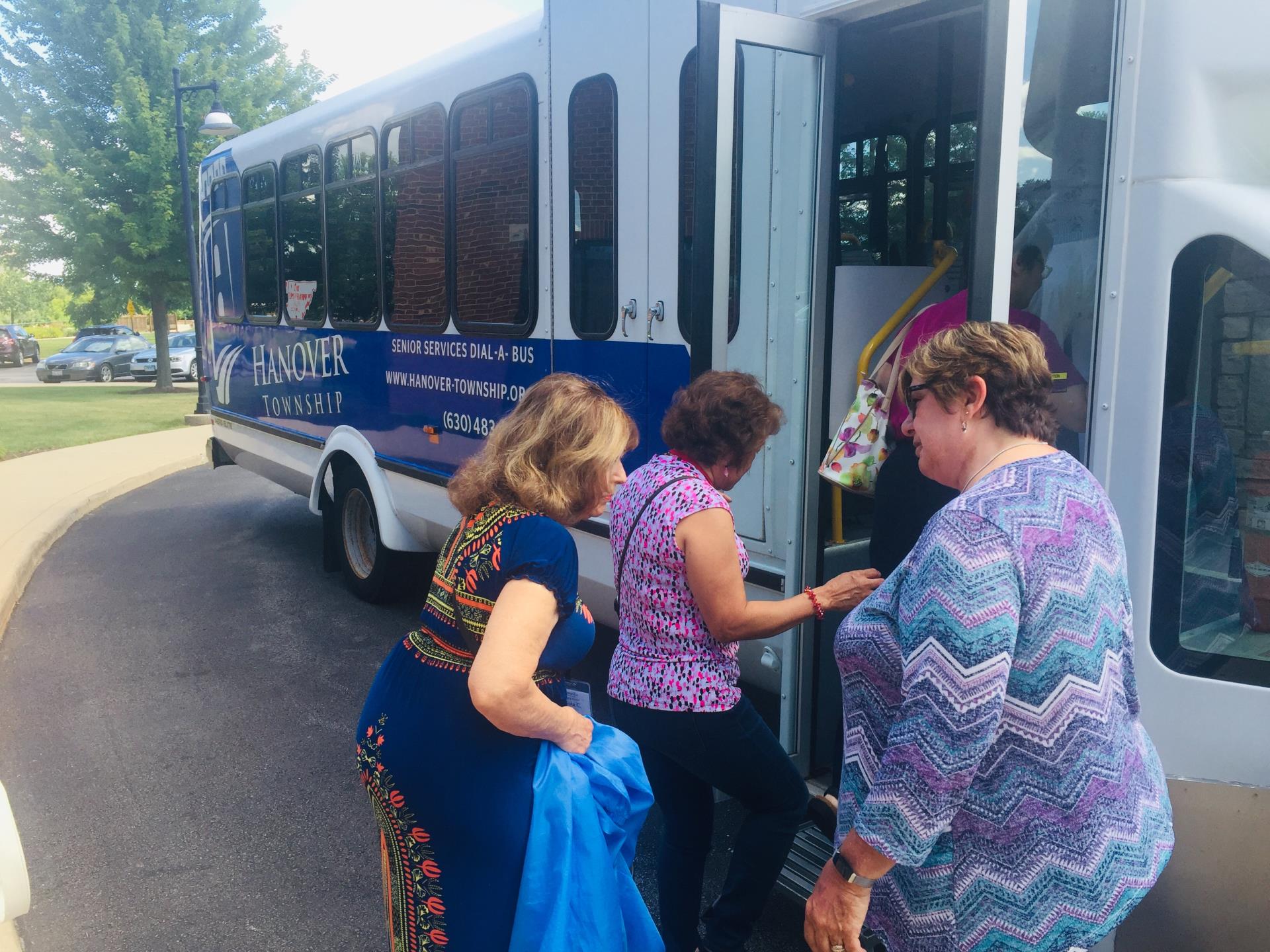 Two female older adults board a township bus with a female staff member looking on.