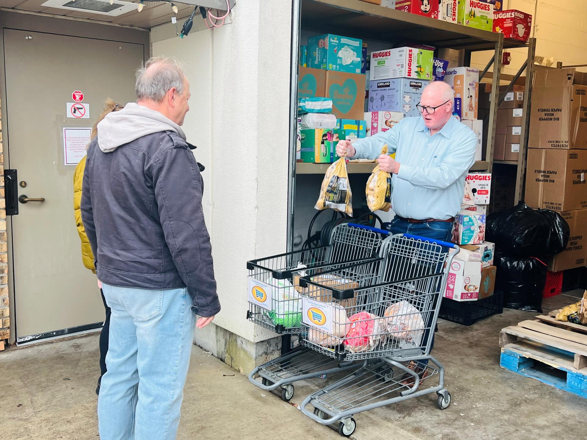 Supervisor McGuire standing behind a shopping cart handing two frozen turkers to a gentleman from inisde an open garage